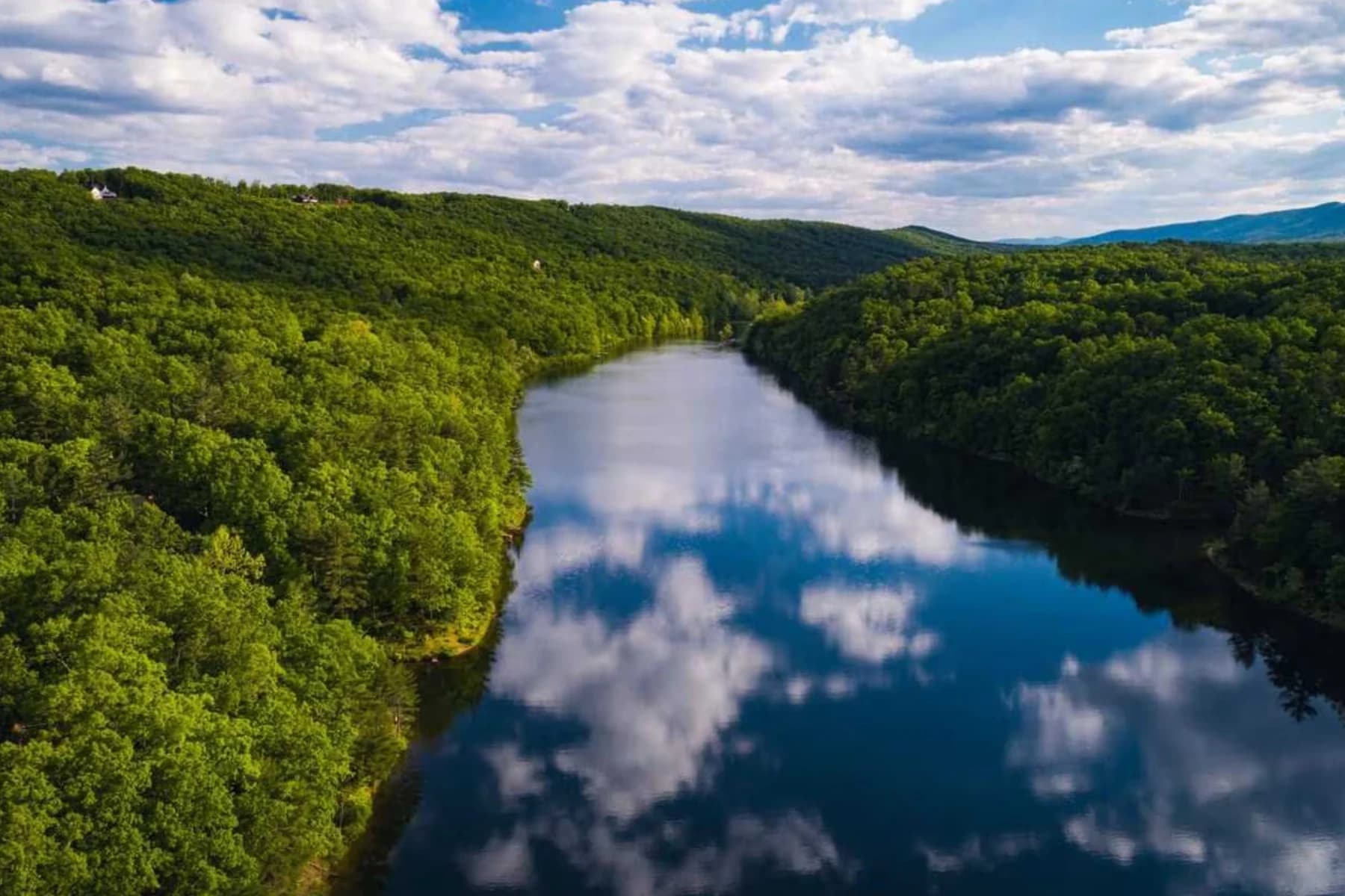 Serene lake surrounded by lush green forests under a partly cloudy sky.