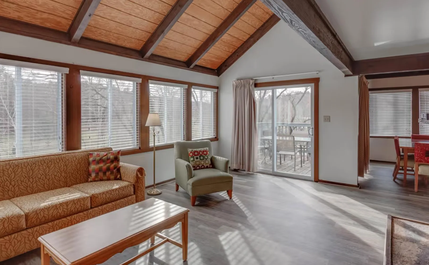 Spacious living room with vaulted ceiling and large windows, featuring cozy furniture and a sliding door to the patio.